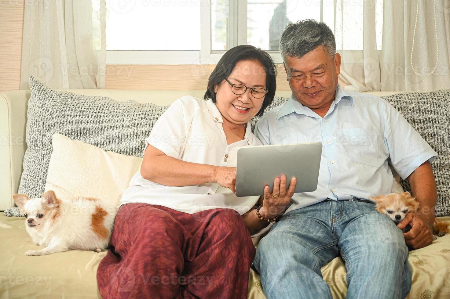Elderly woman and an asian man sitting on a sofa are using a tablet. photo