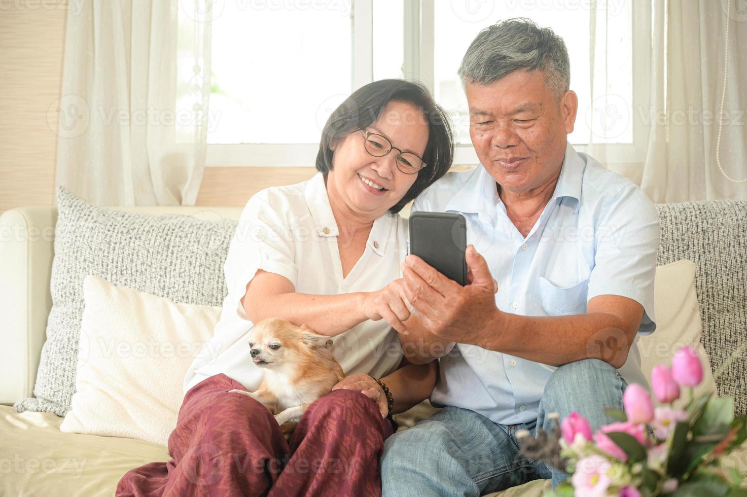 mujeres y hombres asiáticos están sentados en el sofá. están sosteniendo un teléfono inteligente. están sonriendo con una videollamada. foto