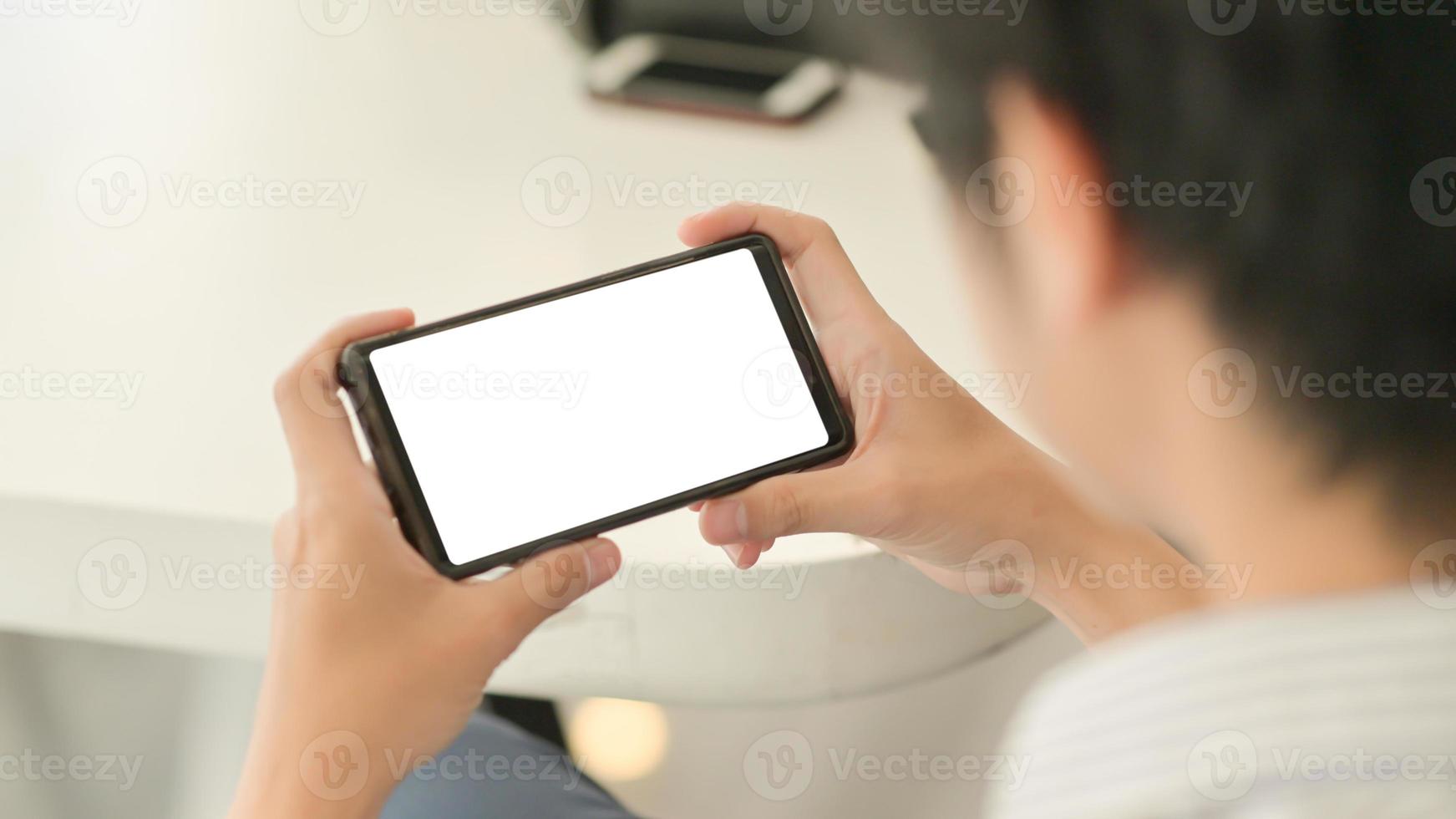 Toma recortada de empresario sosteniendo smartphone de pantalla en blanco horizontal sentarse acostado relajado en una silla en la cómoda oficina. foto