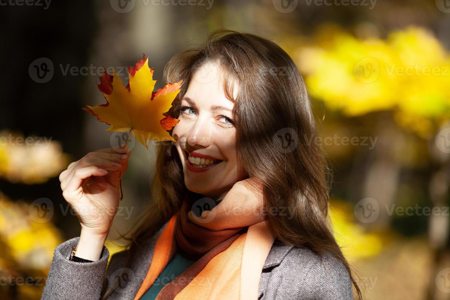 Young woman holding maple leaves in her hand near her face photo