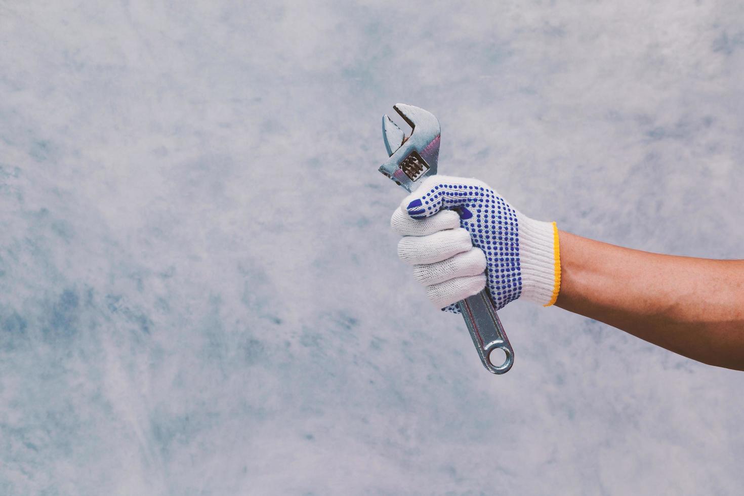 Hand holding a sliding wrench on bare cement wall background photo