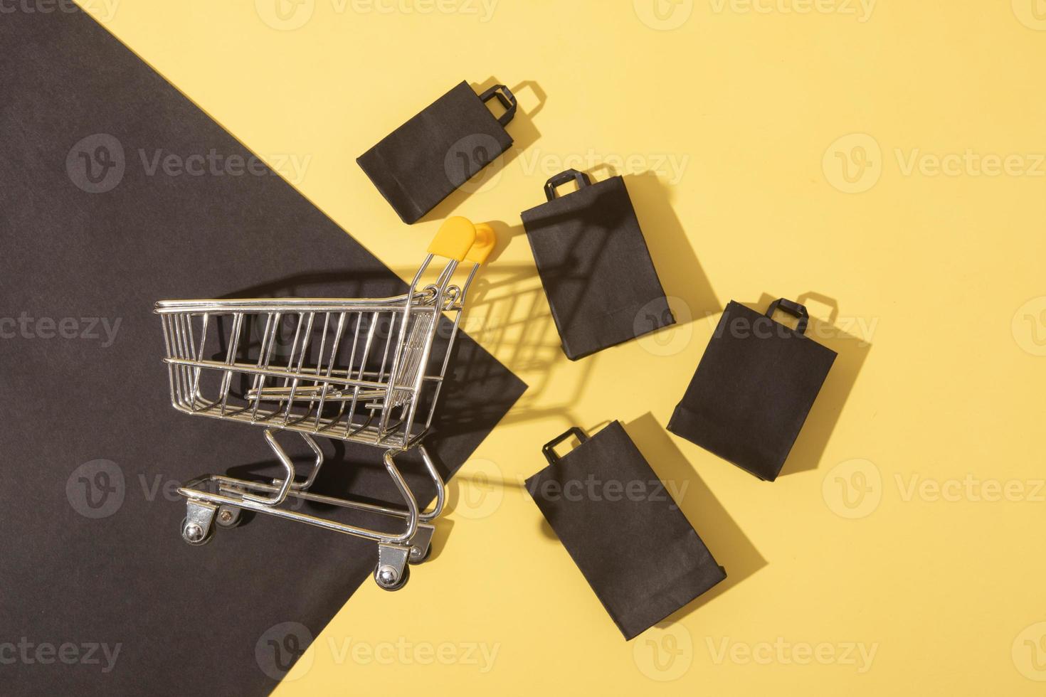 Flat lay miniature supermarket cart with shopping bags in black friday sale on yellow background photo