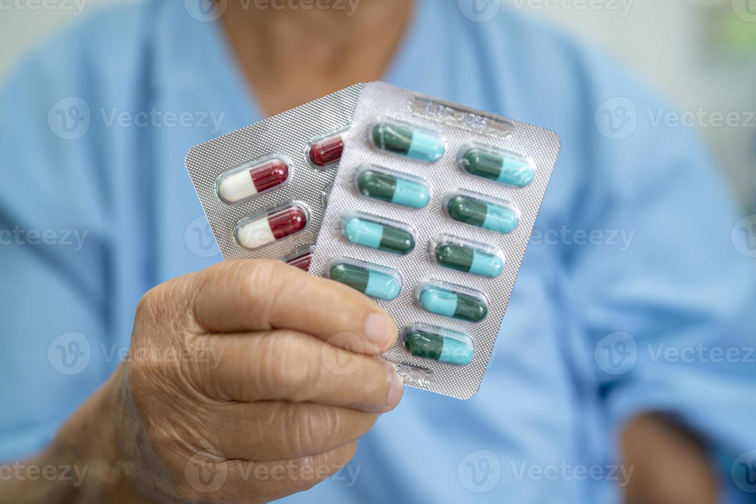 Asian senior woman patient holding antibiotics capsule pills in blister packaging for treatment infection patient in hospital, Pharmacy drugstore concept. Pharmacy drugstore concept. photo