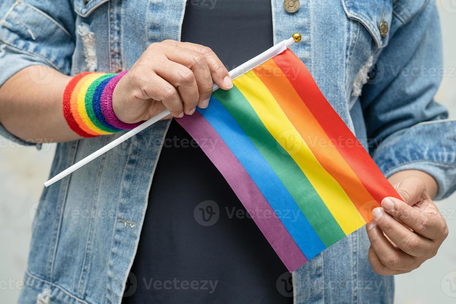 dama asiática con chaqueta de mezclilla azul o camisa de mezclilla y sosteniendo la bandera del color del arco iris, símbolo del mes del orgullo lgbt celebra anualmente en junio las redes sociales de gays, lesbianas, bisexuales, transgénero, derechos humanos. foto