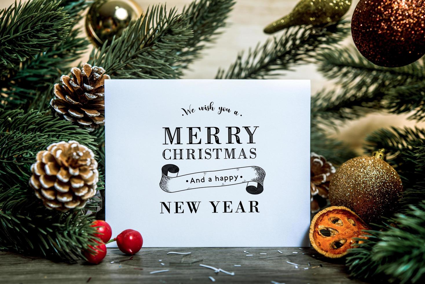 Maqueta de diseño de tarjeta de papel de felicitación navideña con decoración en mesa de madera. foto