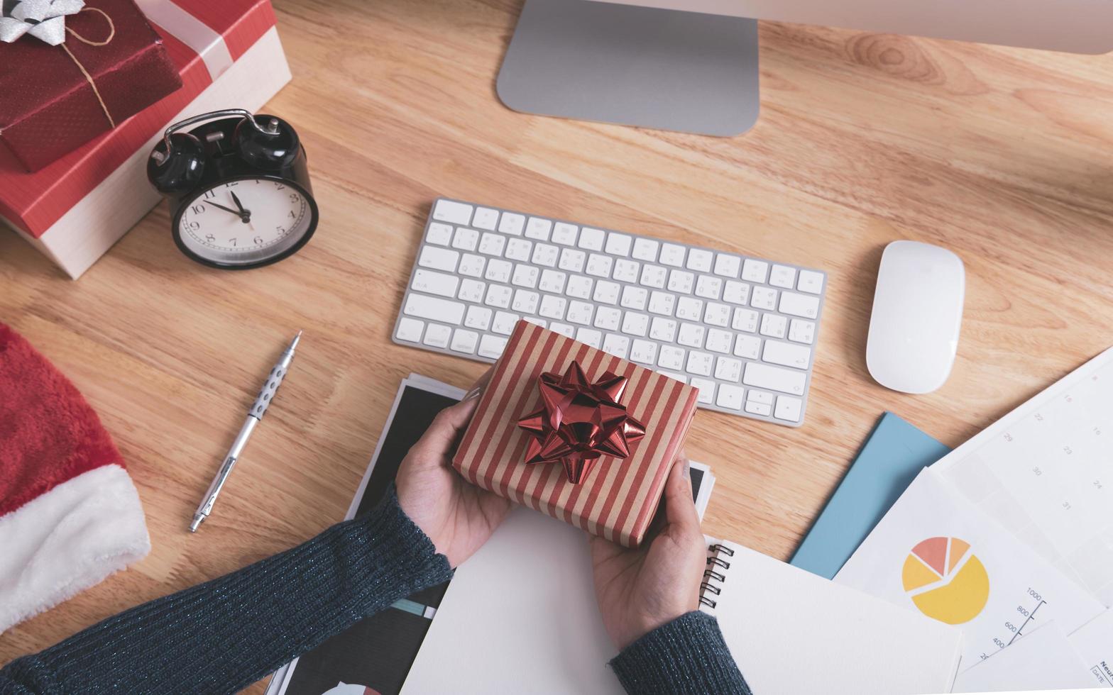 Businesswoman hand holding gift box in christmas holiday at the office with christmas decoration on table. photo