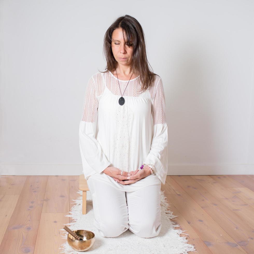 mujer caucásica adulta vestida de blanco durante una sesión de meditación. gong de metal junto a ella. foto