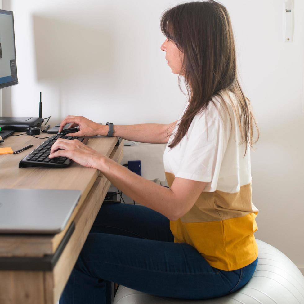 hermosa mujer adulta caucásica que trabaja con una computadora desde su casa. sentado en una pelota de estabilidad foto