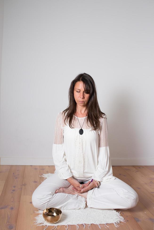 Beautiful adult woman dressed in white during a meditation sesion. Sitting cross legged yoga pose. Cupper singing bowl. photo