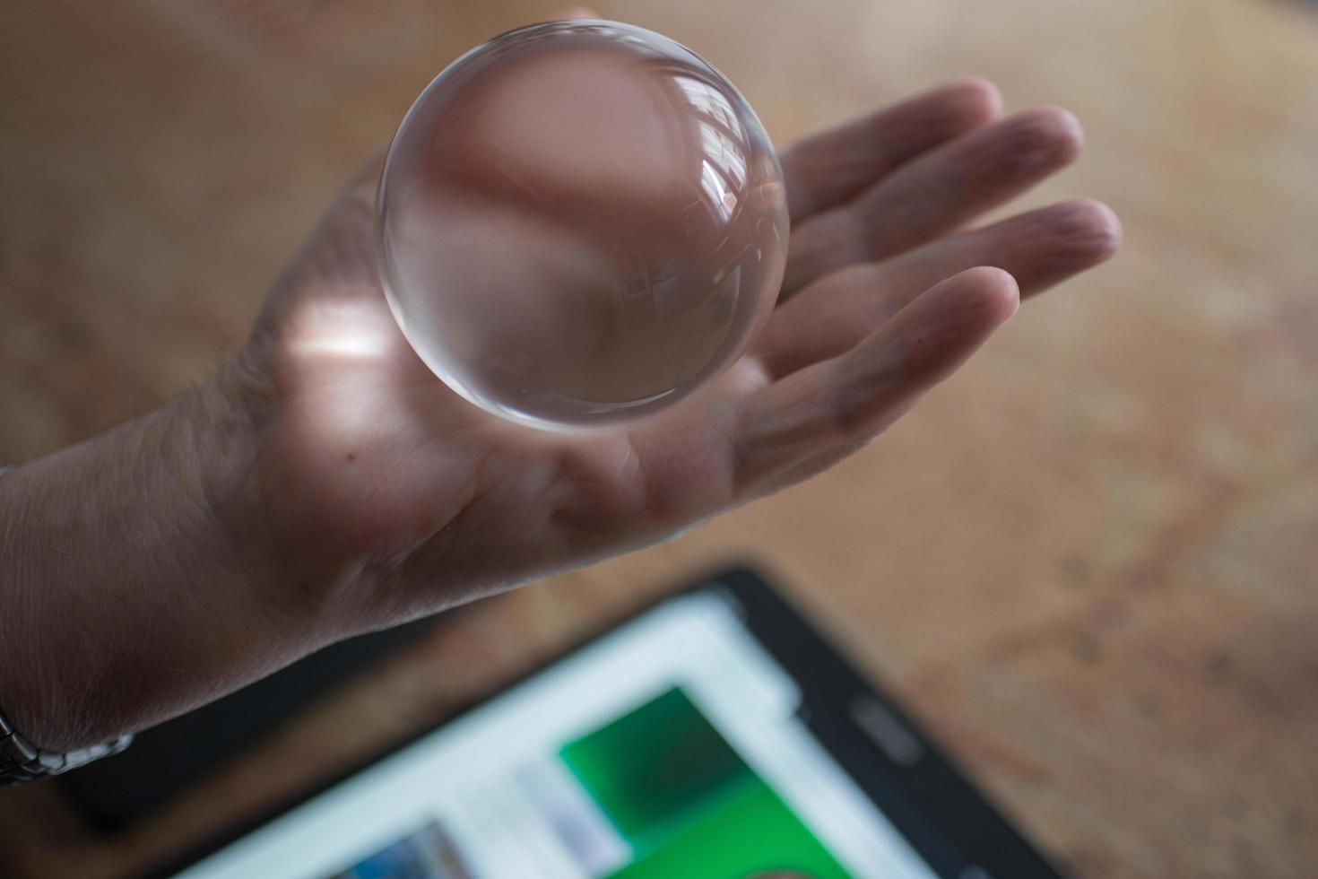 Close up of an aged man hand holding a crystal ball. Tablet with news  in the background. Concept uncertain future photo