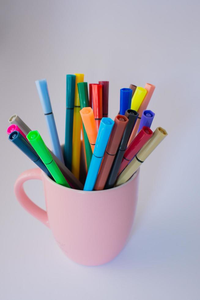 taza rosa llena de marcadores de colores. Fondo blanco foto