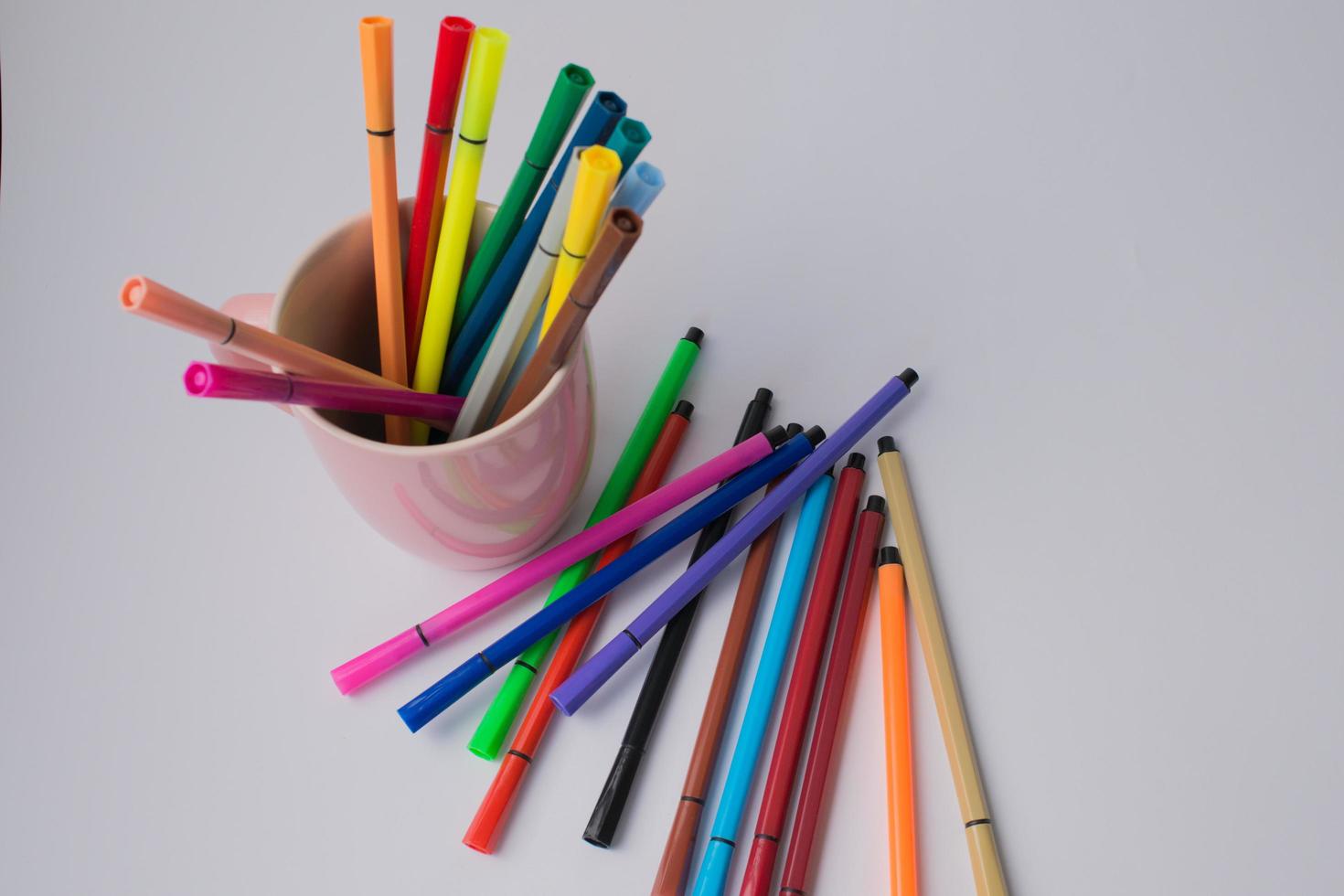 Pink cup with colorful markers and some others on a white surface photo