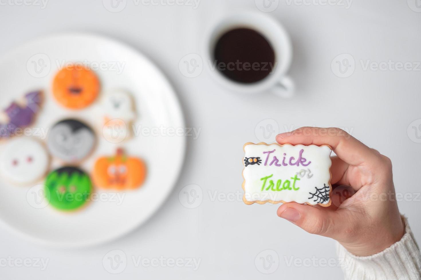 woman hand holding funny Halloween Cookie during drinking coffee. Happy Halloween day, Trick or Threat, Hello October, fall autumn, Traditional, party and holiday concept photo