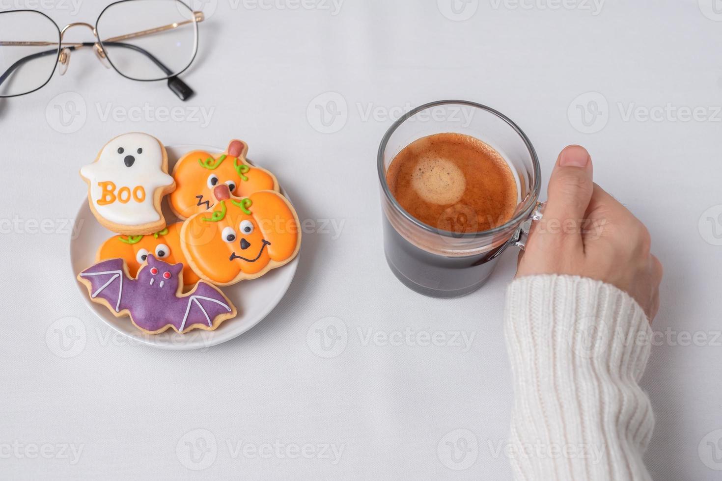 woman hand holding coffee cup during eating funny Halloween Cookies. Happy Halloween day, Trick or Threat, Hello October, fall autumn, Traditional, party and holiday concept photo