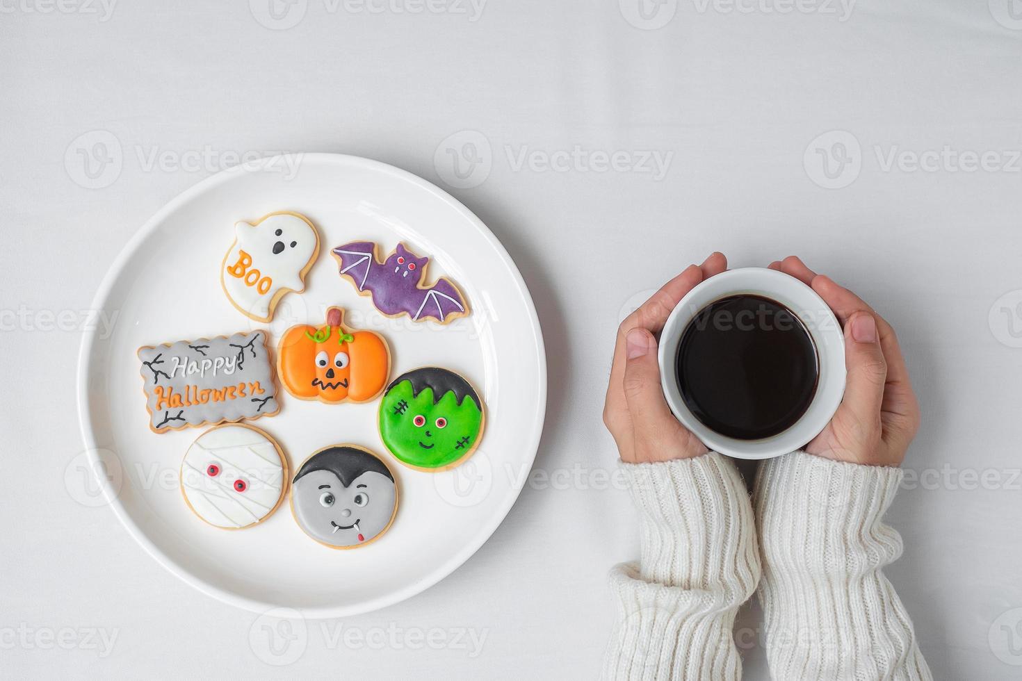 mano de mujer sosteniendo la taza de café durante la comida divertidas galletas de halloween. feliz día de halloween, truco o amenaza, hola octubre, otoño otoño, tradicional, concepto de fiesta y vacaciones foto