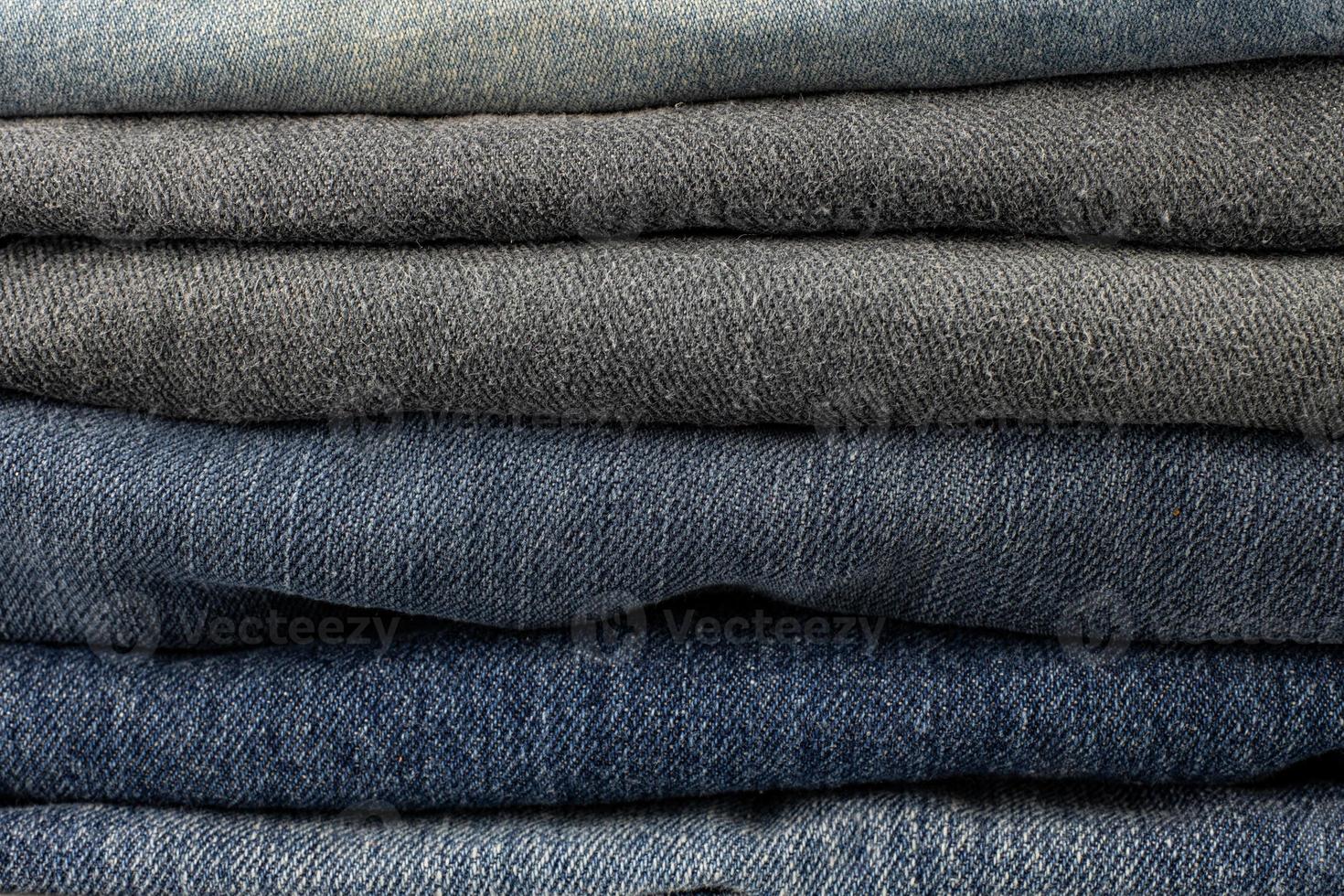 Stack of various shades of blue jeans trousers at white background photo