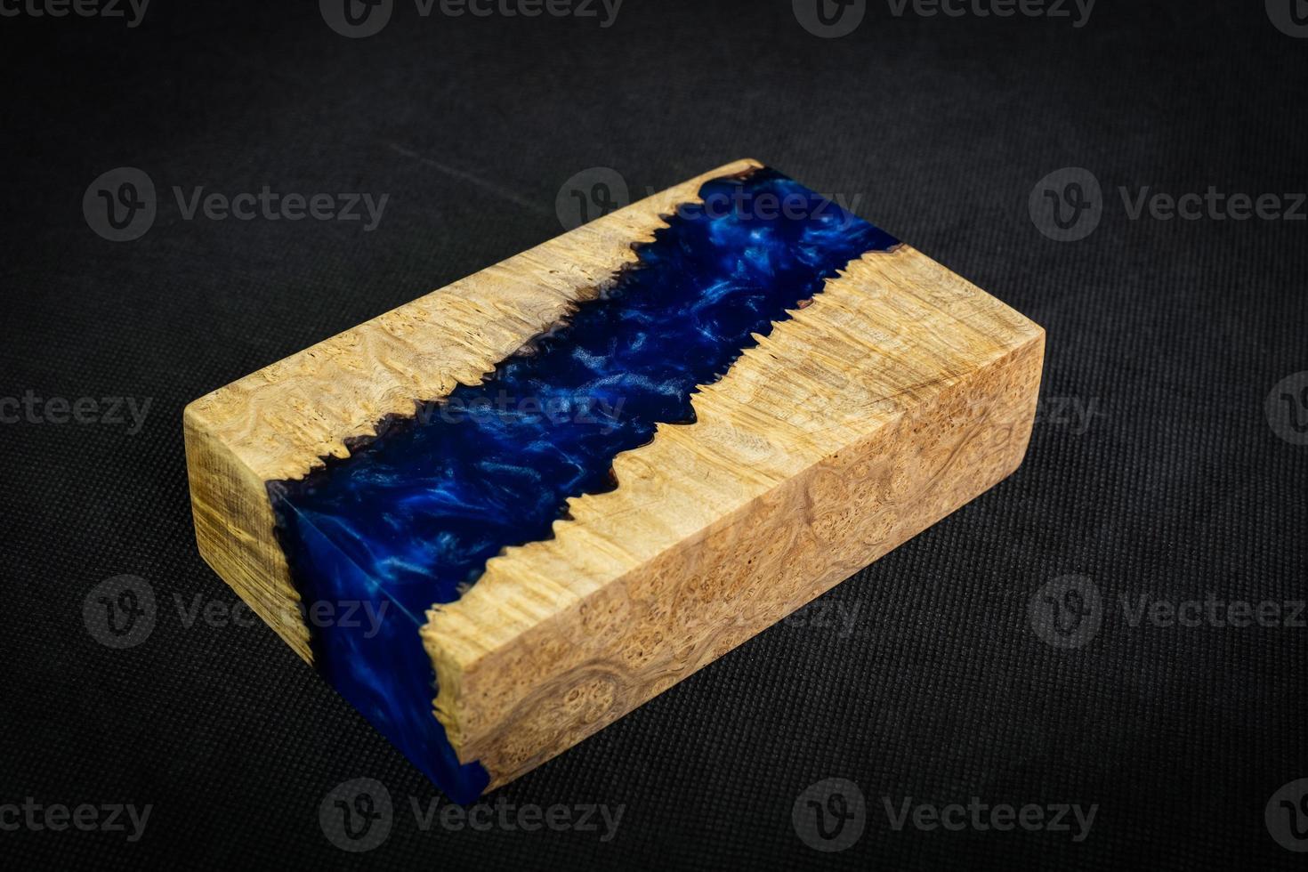 Casting blue epoxy resin with nature burl maple wood cube on black background photo