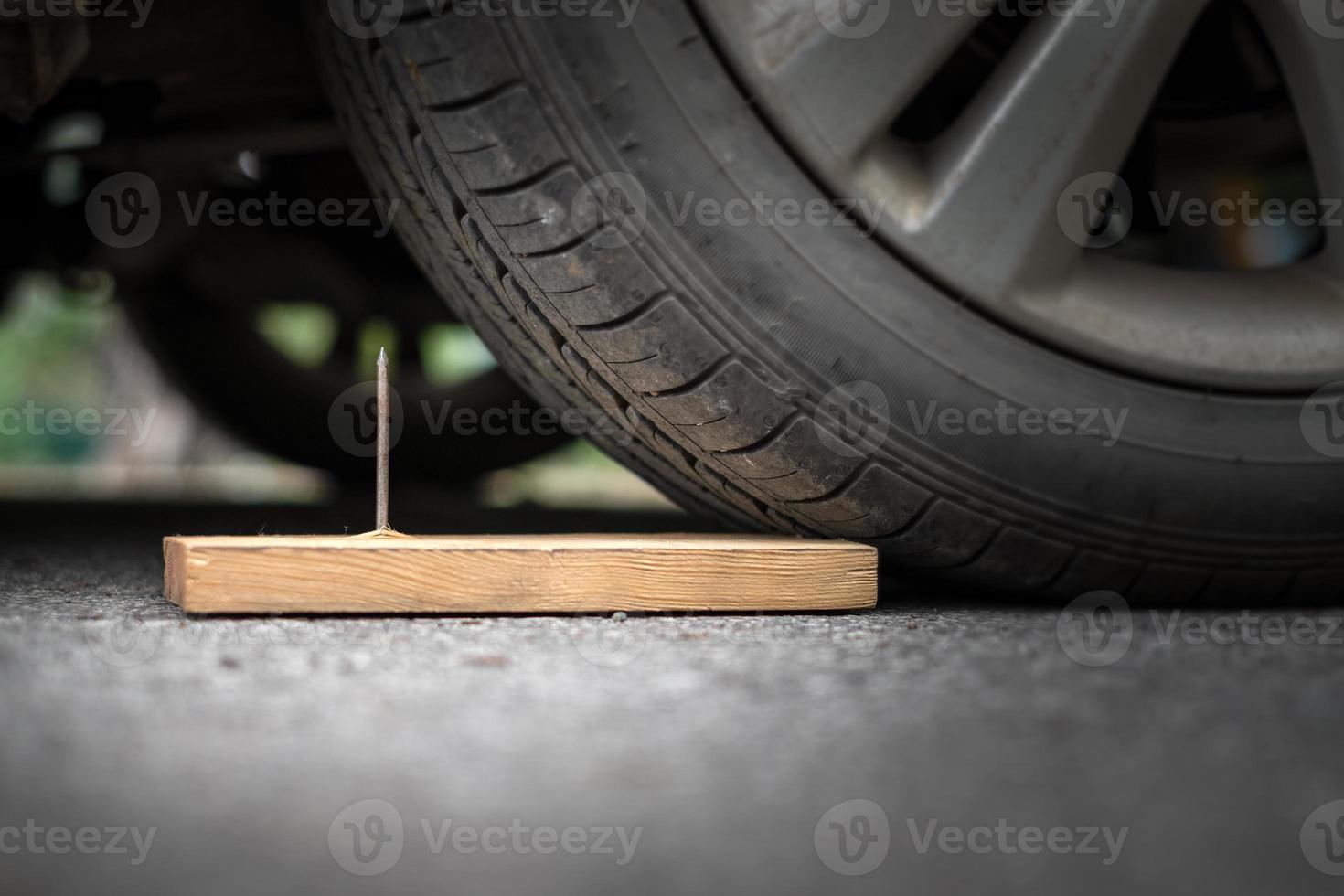 Close up a metal nail on board wood nearly to puncture into wheel tire photo