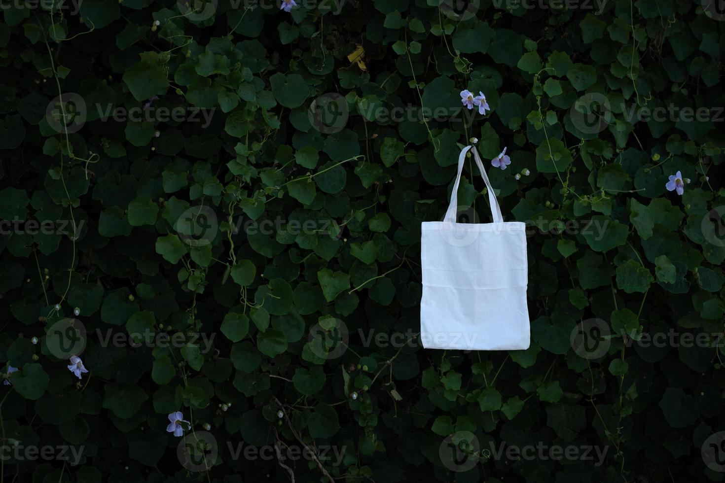 Totalizador de bolsa de tela de tela blanca en blanco en el fondo de follaje de árboles de arbusto verde, concepto de reciclaje de conservación del medio ambiente foto