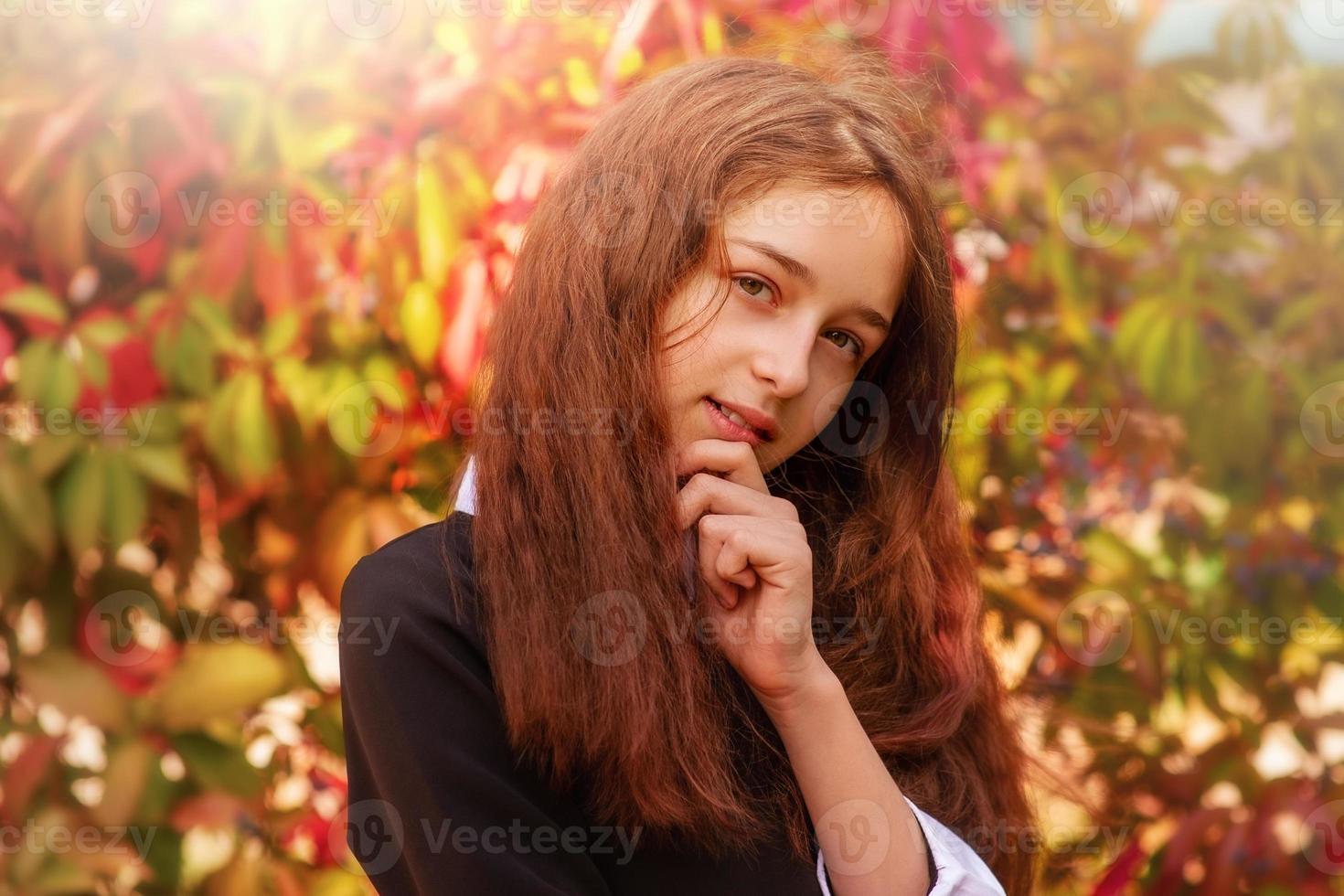 Portrait of a girl 11 years old with long hair in the fall on a background of red leaves. Schoolgirl photo