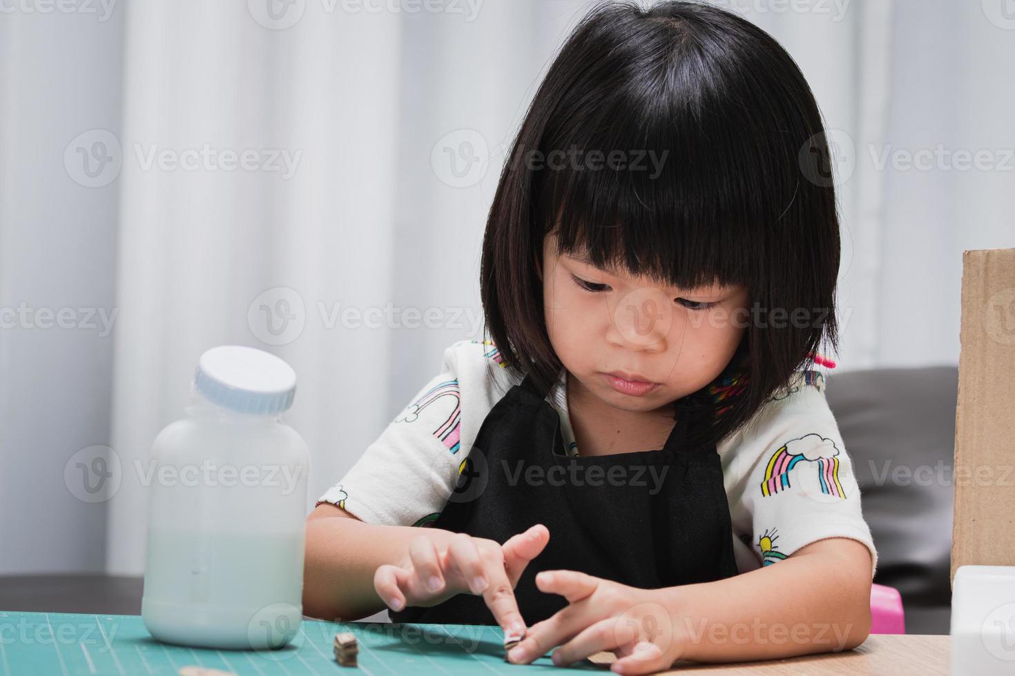 Little child uses her little hands to glue a small piece of cardboard to put together a craft. Children enjoy learning to create things. Work to send teachers according to the lessons. photo