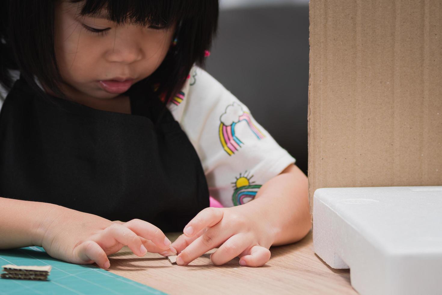 Retrato de niño aprende a hacer pegamento pegado. niño en edad preescolar poniendo pegamento en barra de cartón para la tarea escolar. niña usando sus manos haciendo un dulce hogar para el proyecto de bricolaje. enfoque selectivo. foto