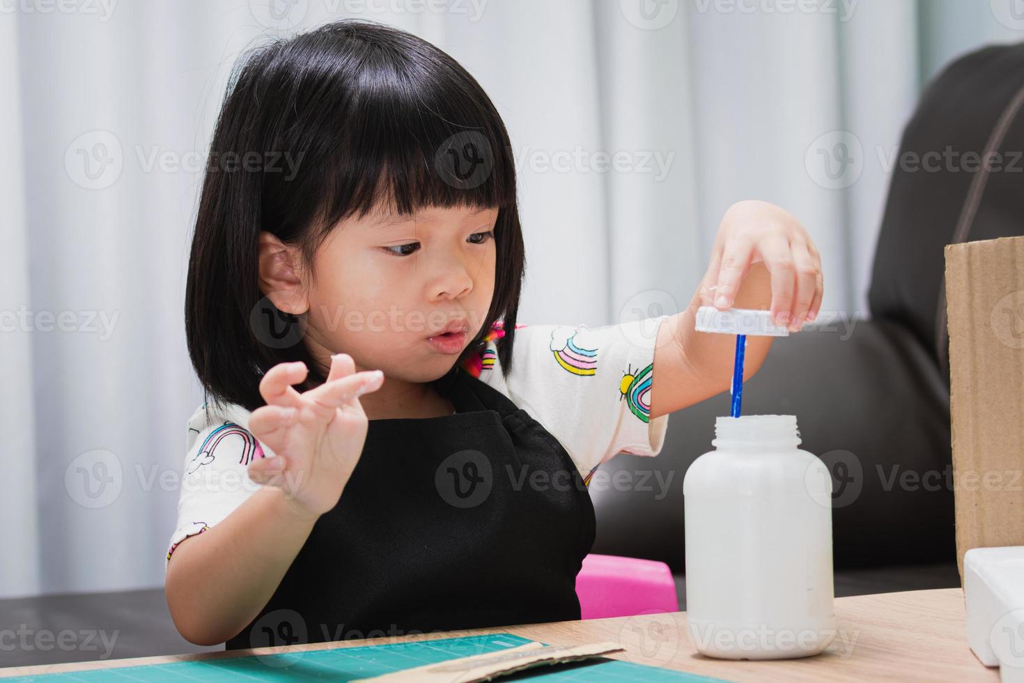 Una niña de kindergarten haciendo manualidades muestra expresiones emocionadas cuando abre las tapas de las botellas de pegamento, el niño se envuelve la boca y se divierte haciendo sus propias creaciones. niños de 4 a 5 años. foto