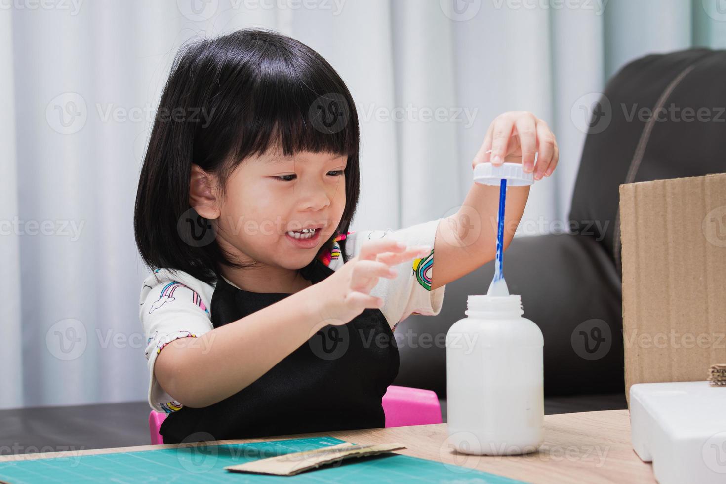 Child are having fun learning through hobbies with arts and crafts, gluing waste paper boxes with glue, imaginative creations, smiling sweet children, kid girl poking their fingers into glue tubes. photo