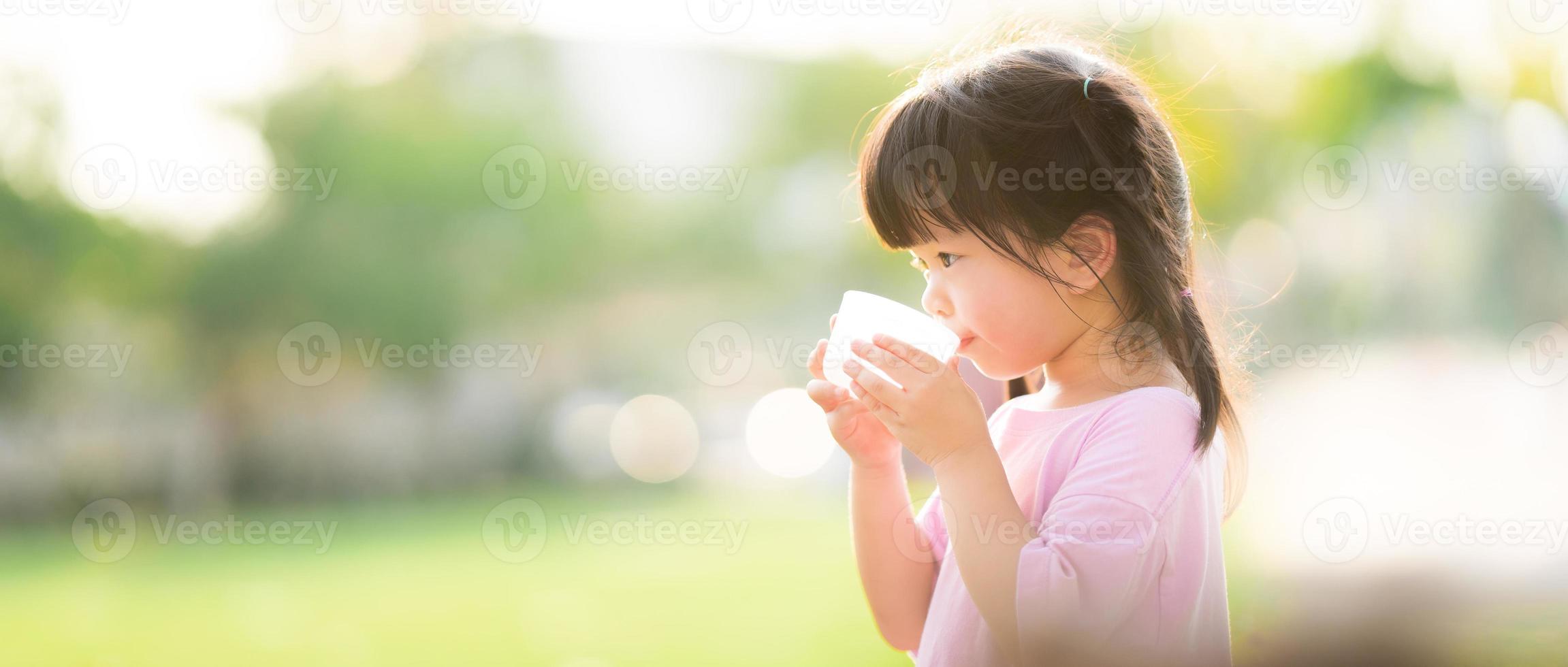 Concept of water are great for kid. Child are drinking from plastic glasses. Natural background. During the summer or spring. The side of a 4 year old girl. photo