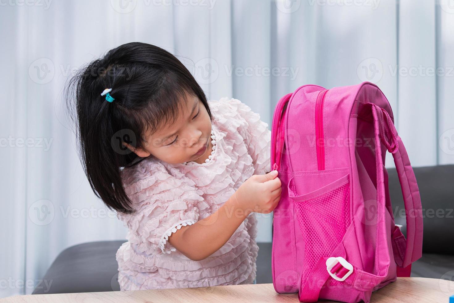 Preschool girl is zipping her school bag to prepare her belongings for back to school. Cute kid, age 4-5 years old. photo