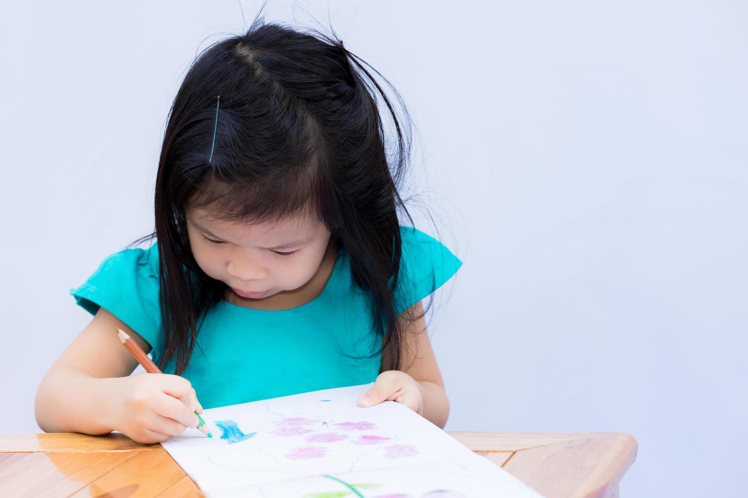 una alumna asiática de 3 a 4 años hace arte y pinta madera con lápices de colores de dos colores. los niños lindos aprenden en casa. los niños en edad preescolar disfrutan del arte. Fondo de pared blanca aislada. foto