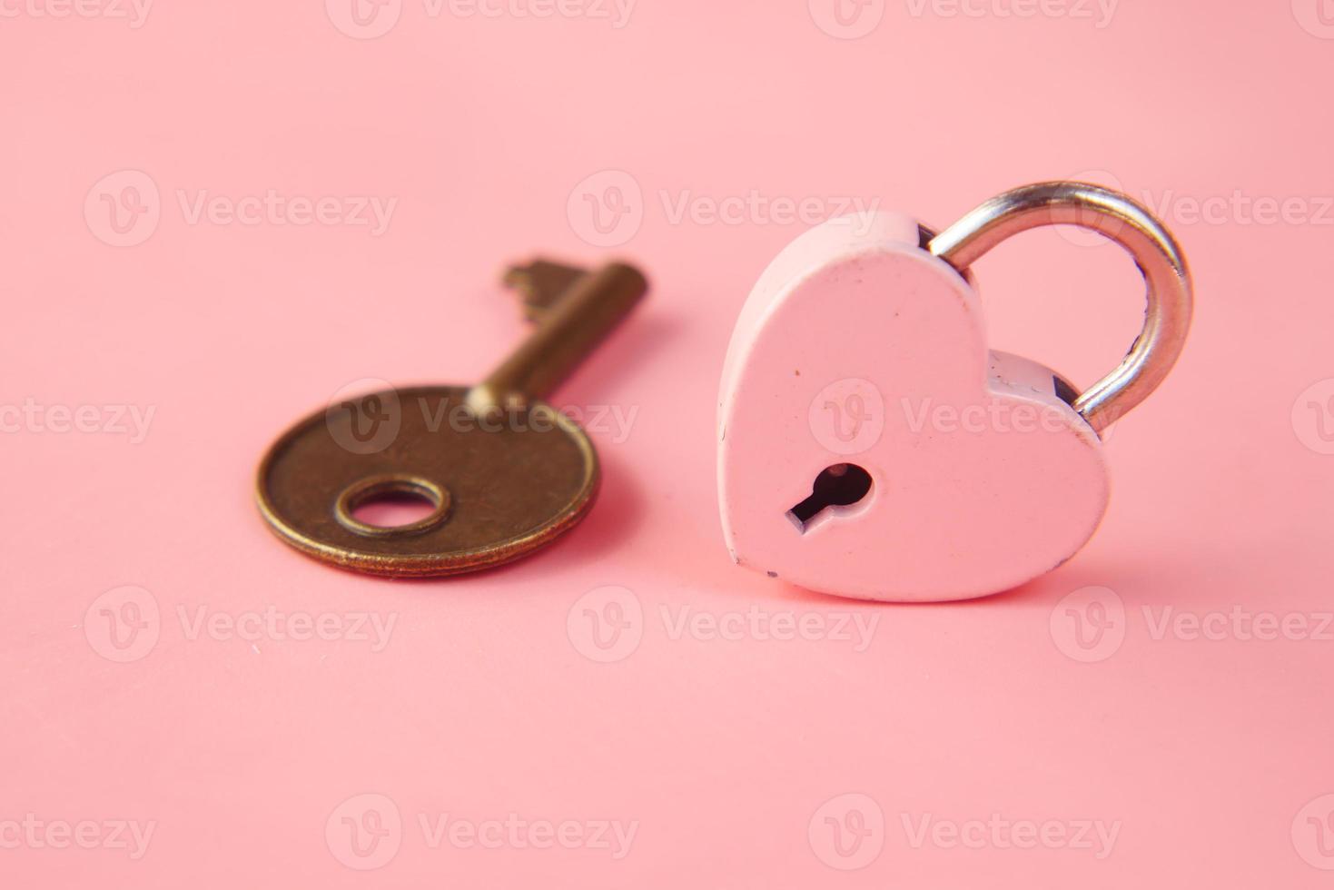Candado con forma de corazón rosa y llave en la mesa foto