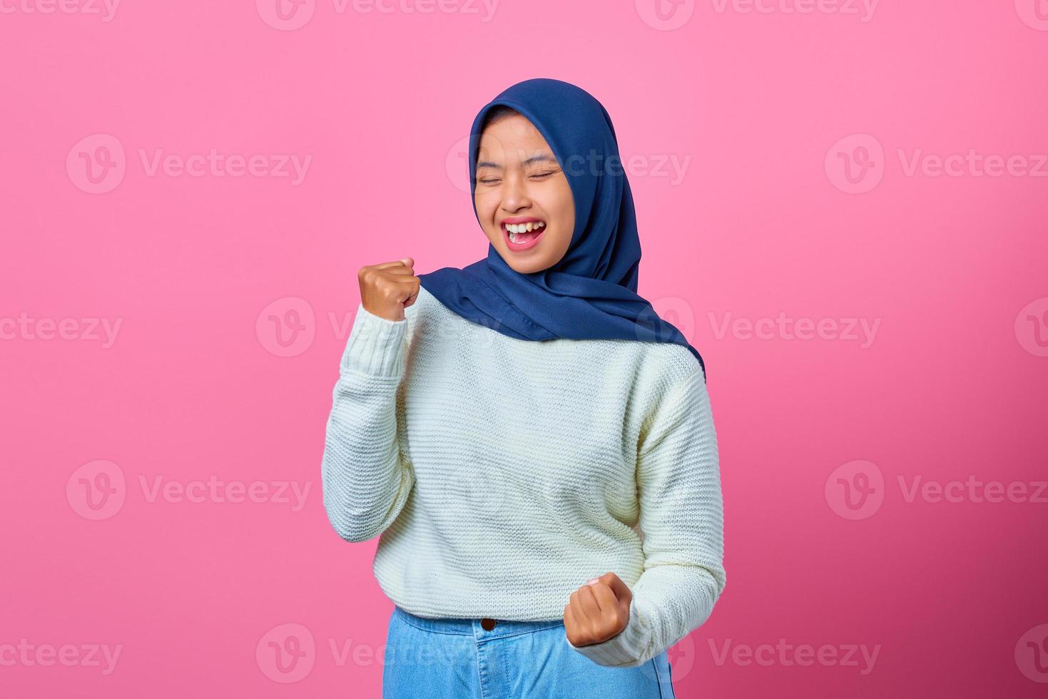 Portrait of excited young Asian woman celebrating success with raised arms photo