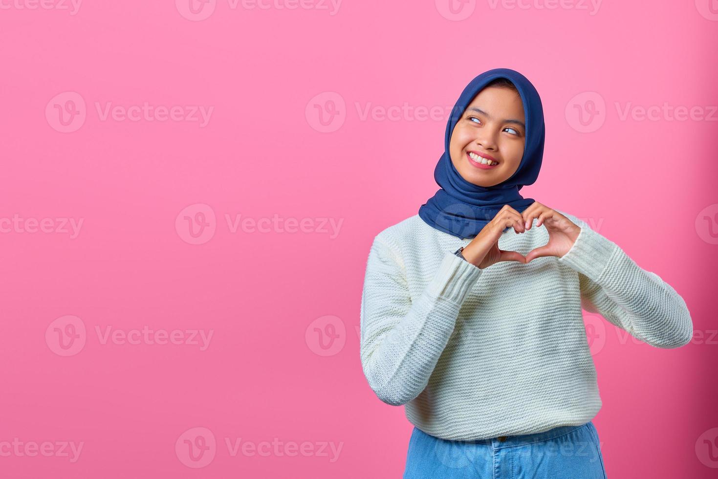 Portrait of smiling young Asian woman showing heart shape gesture with two hands photo