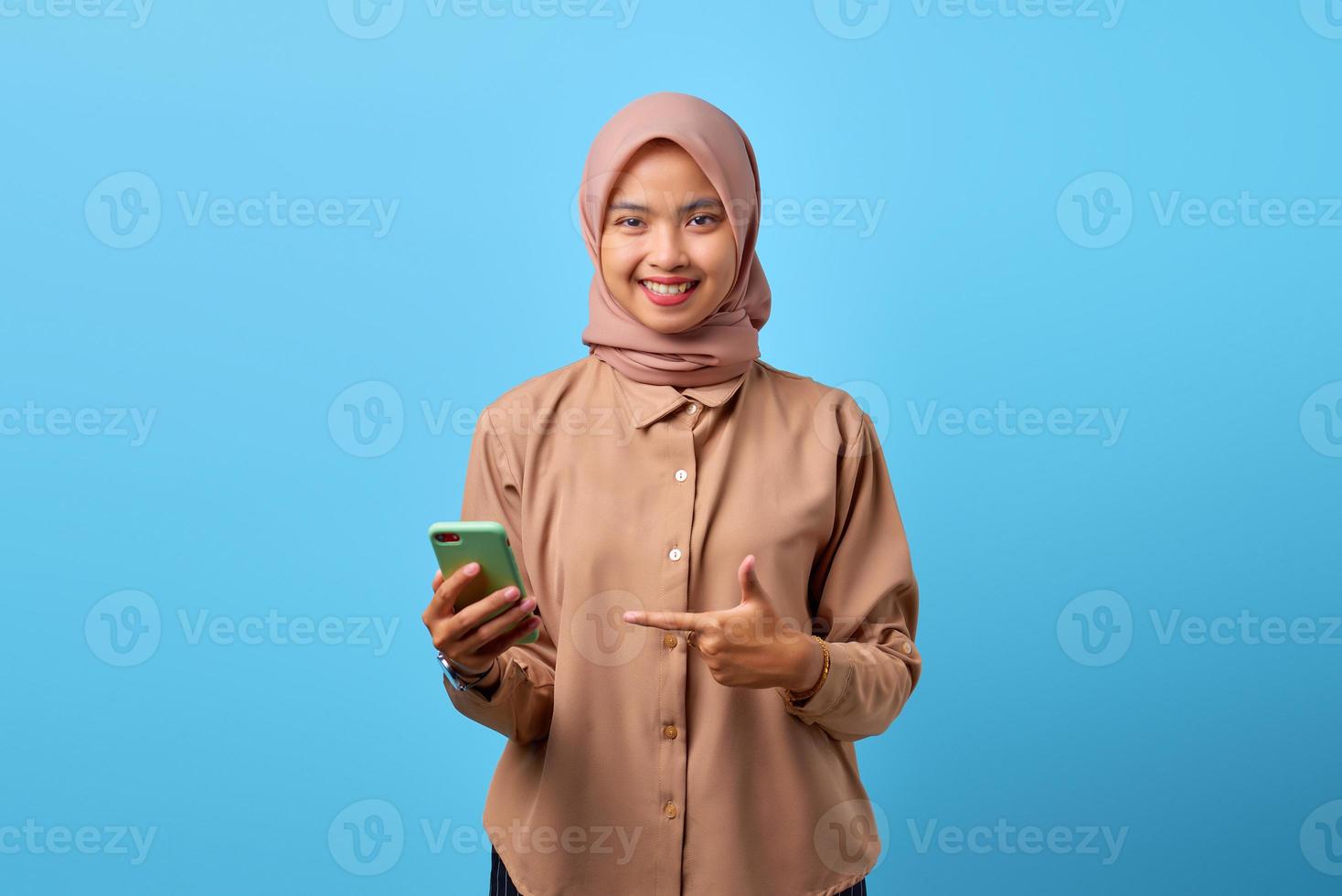 Portrait of smiling young Asian woman pointing on mobile phone with finger photo