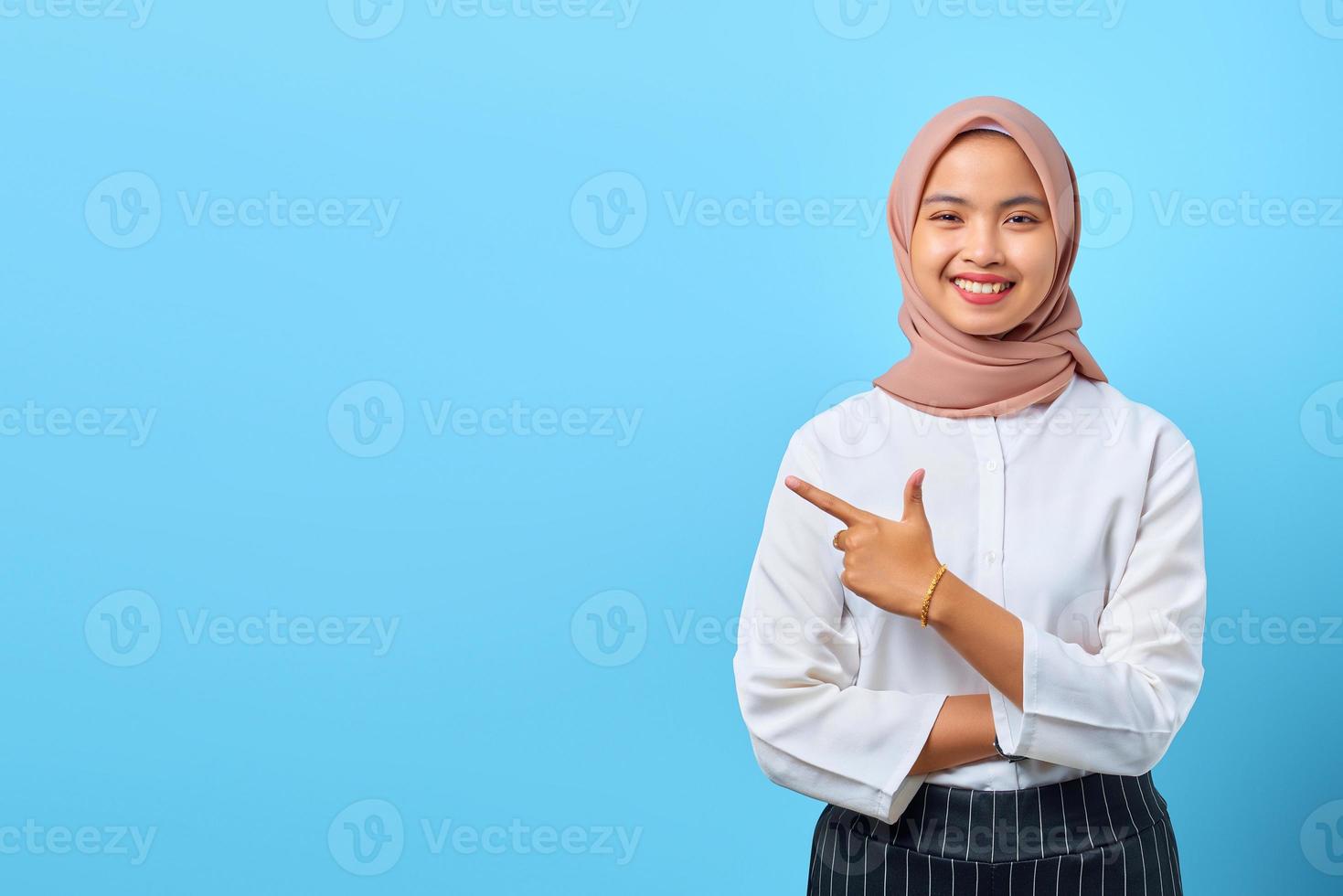 Retrato de una mujer asiática joven sonriente con los brazos cruzados y apuntando al espacio vacío foto