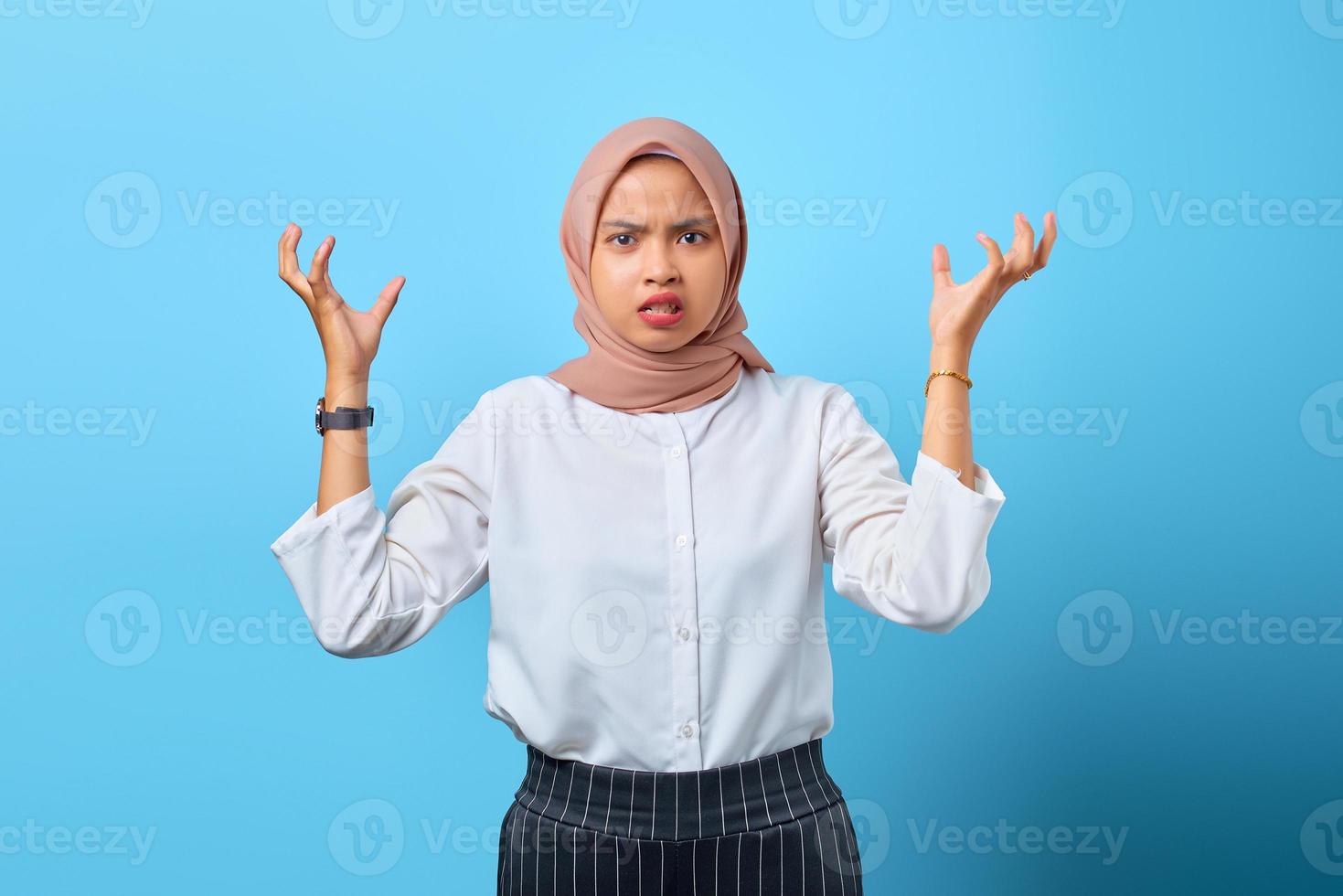 Retrato de mujer asiática joven enojada molesta con el argumento con las manos levantadas sobre fondo azul. foto