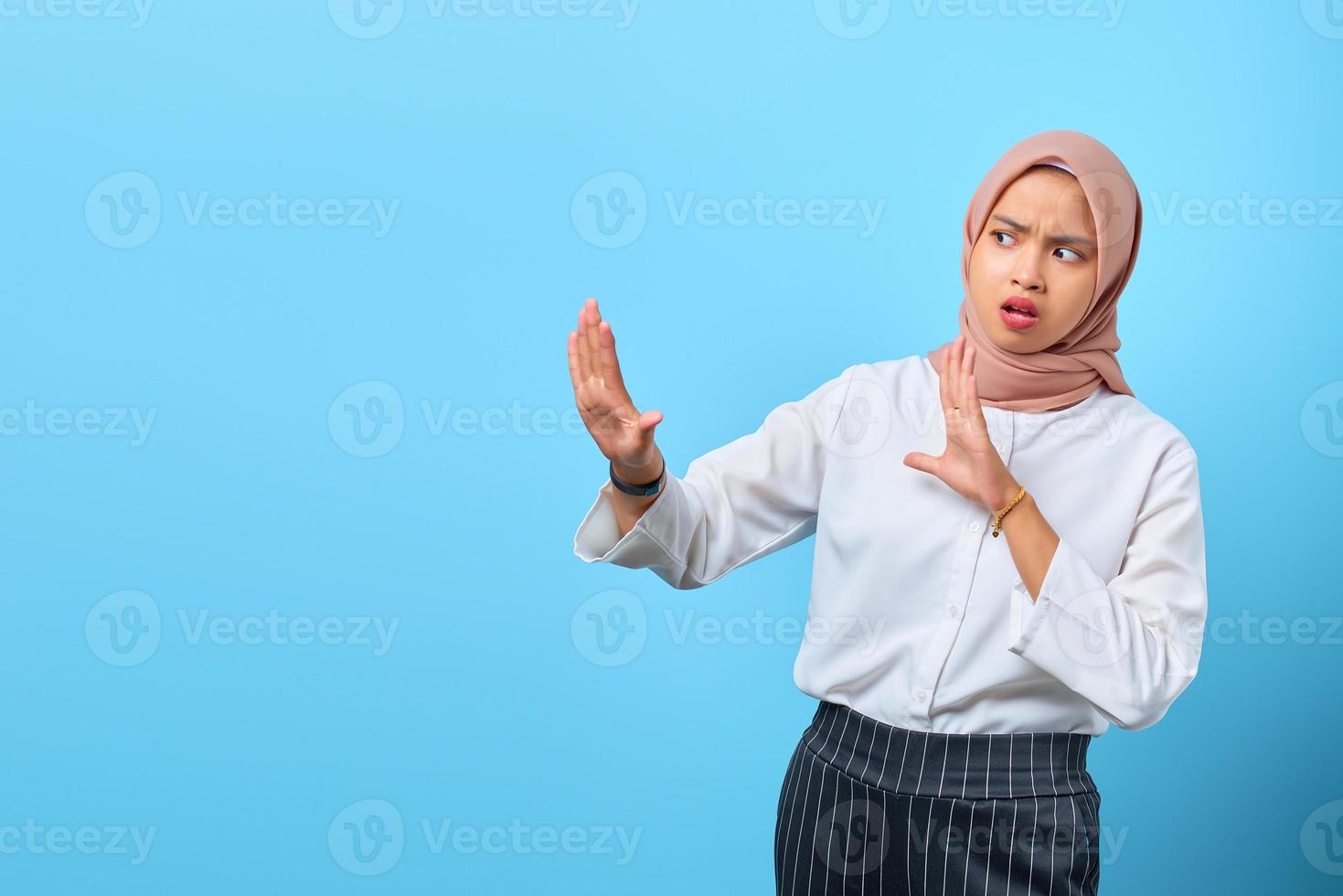 Portrait of nervous anxious young Asian woman make stop don't move gesture over blue background photo