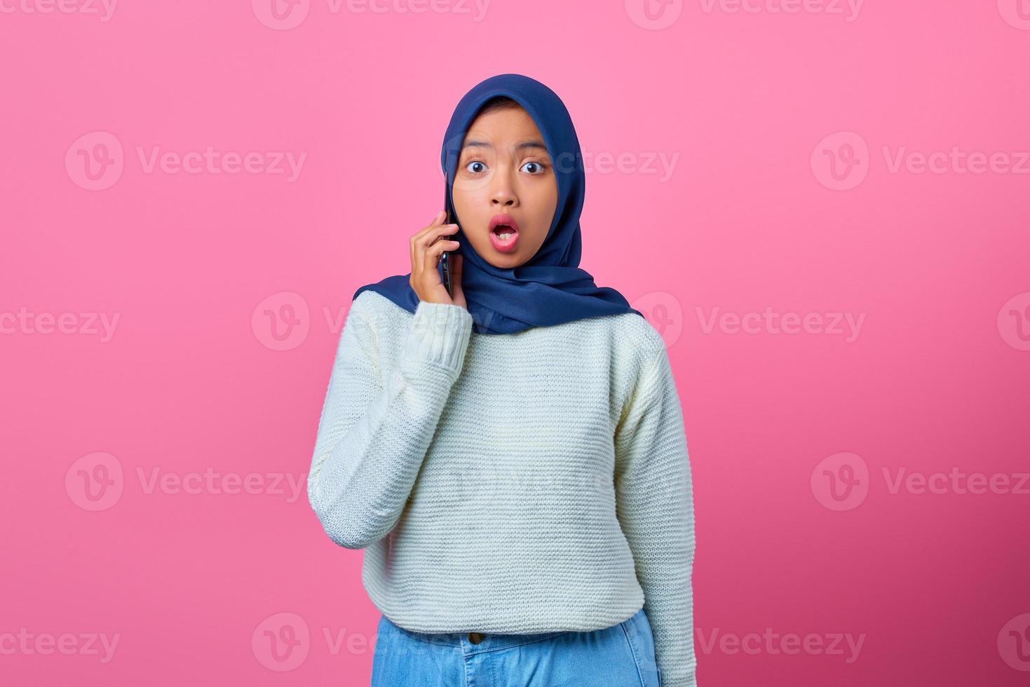 Retrato de mujer asiática joven sorprendida hablando por teléfono inteligente sobre fondo de color rosa foto