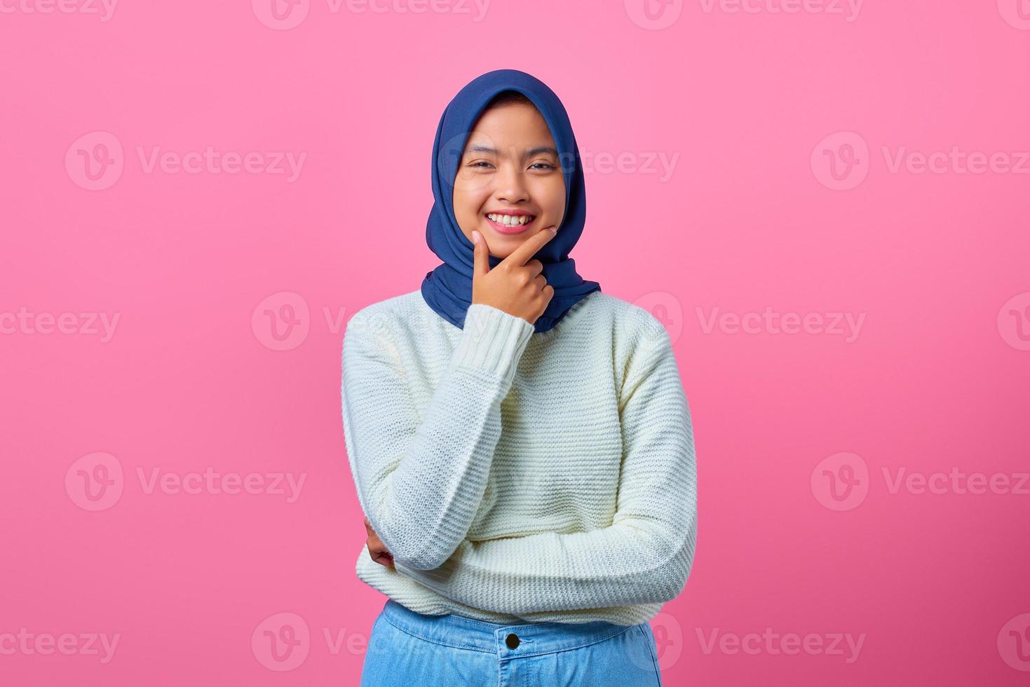 Retrato de mujer asiática joven sonriente tocando la barbilla con la mano sobre fondo de color rosa foto