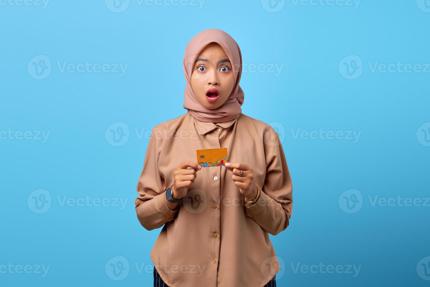 Portrait of shocked young Asian woman holding credit card while looking at camera photo