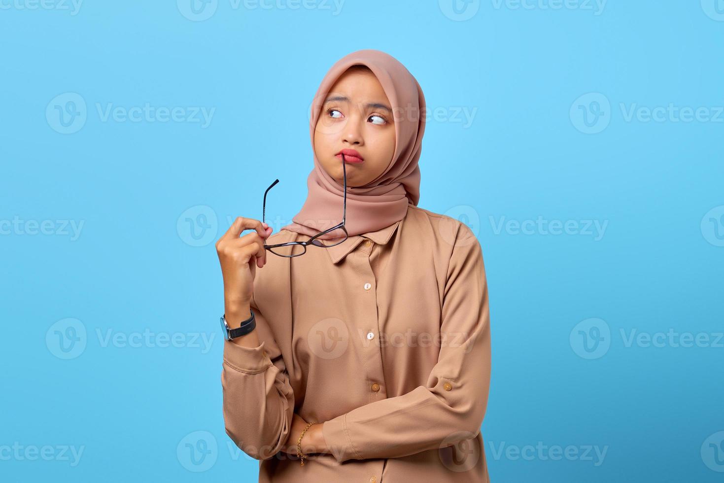 Portrait of thinking young Asian woman biting eyewear and look to empty space photo