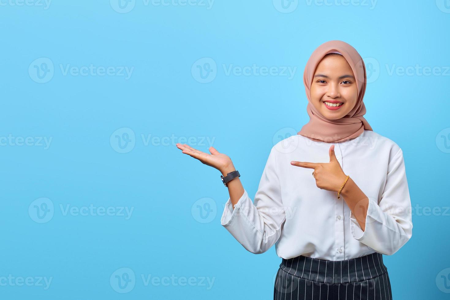 Retrato de mujer asiática joven sonriente mientras presenta el producto y apunta con el dedo foto