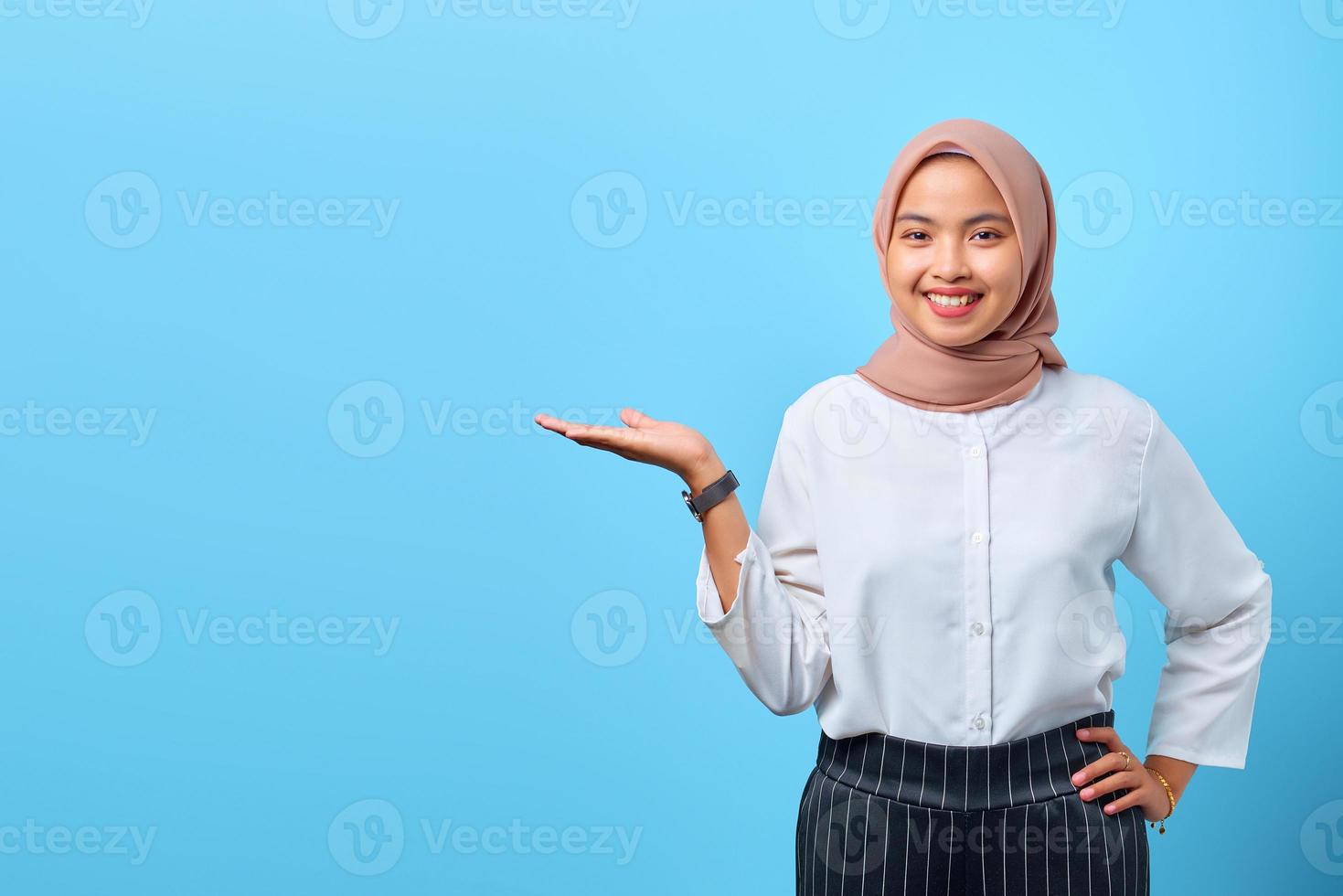 Retrato de mujer asiática joven sonriente que presenta el producto sobre fondo azul. foto