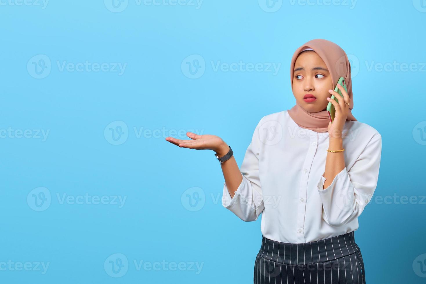 retrato, de, triste, joven, mujer asiática, hablar teléfono, con, manos levantadas, encima, fondo azul foto