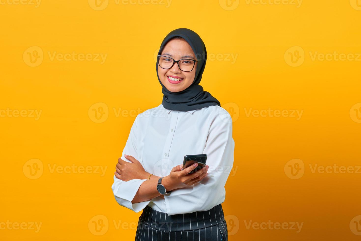 Smiling young Asian woman using mobile phone and texting message on yellow background photo