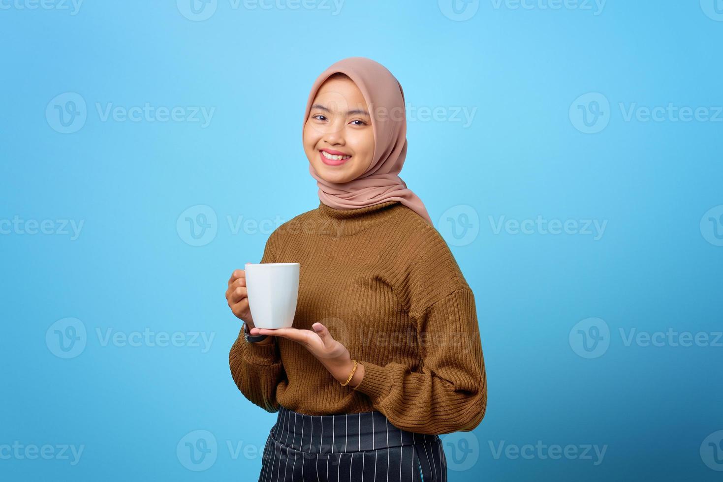 Beautiful young Asian woman holding mug and drinking tea on blue background photo