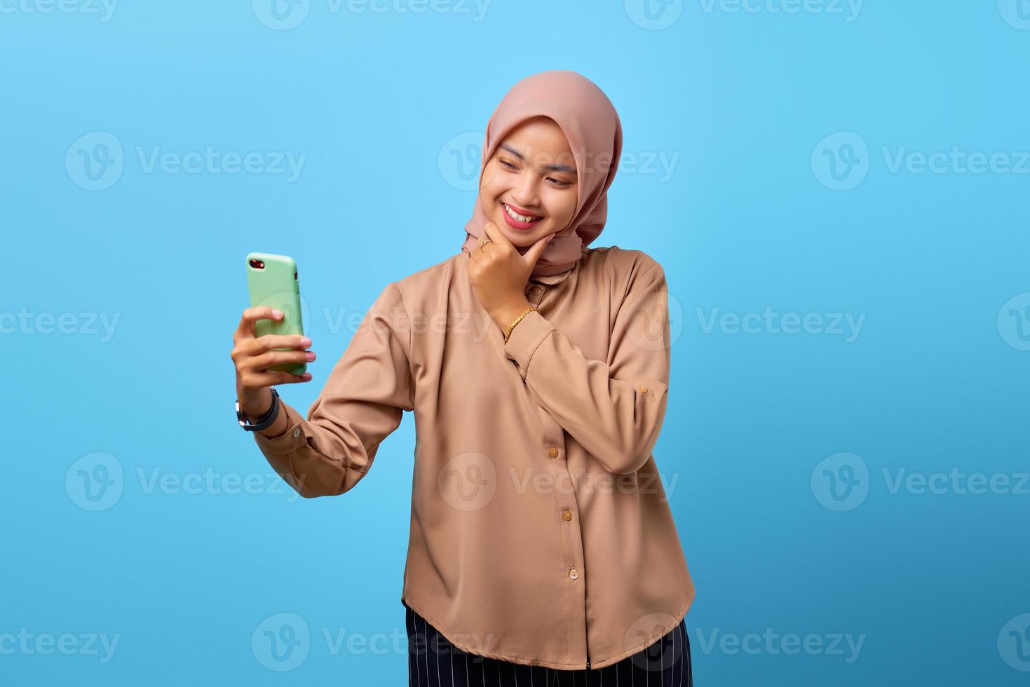 retrato, de, alegre, joven, mujer asiática, mirar, teléfono móvil, con, entregue barbilla foto