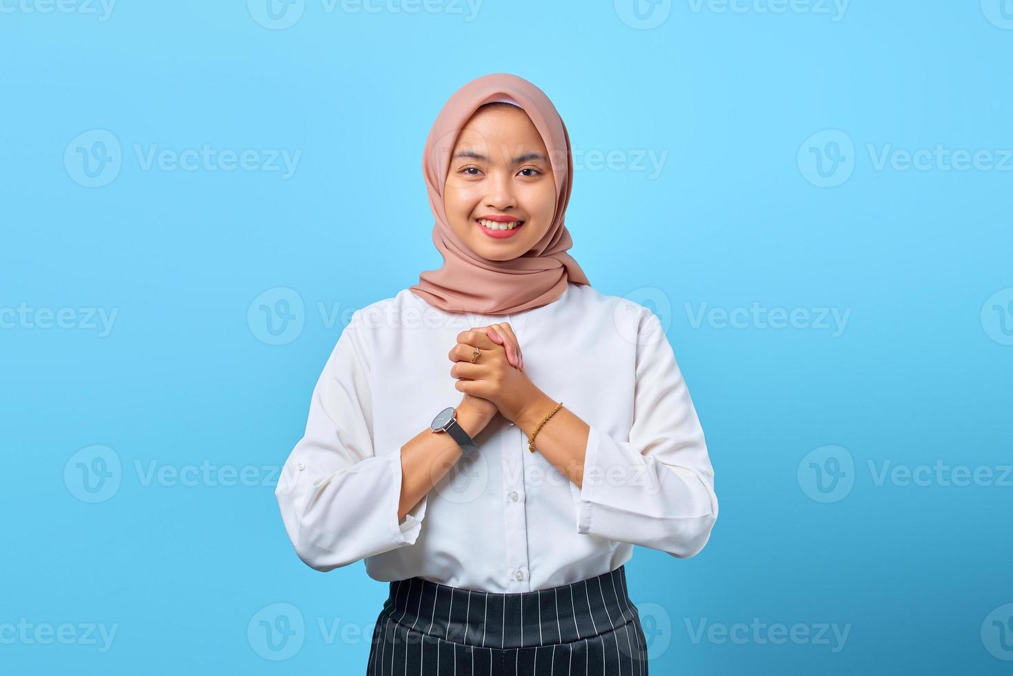 Portrait of cheerful young Asian woman putting hands together over blue background photo