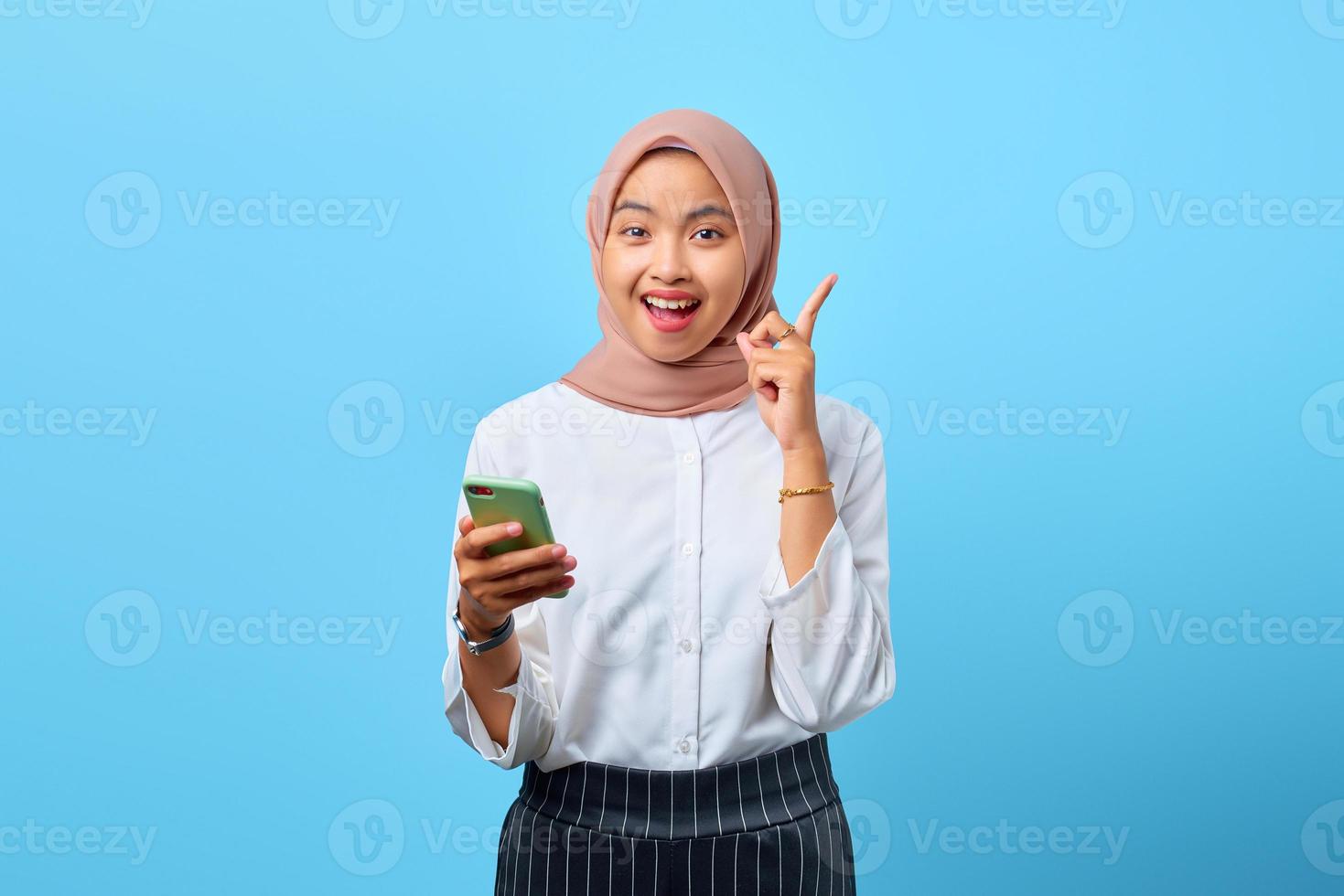 Portrait of excited young Asian woman holding mobile phone and raised finger because have solutions photo